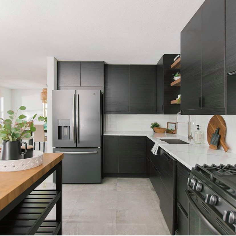Skandinavisk inredning av ett litet vit vitt kök, med en nedsänkt diskho, släta luckor, svarta skåp, bänkskiva i kvarts, vitt stänkskydd, svarta vitvaror, klinkergolv i keramik, en köksö och grått golv