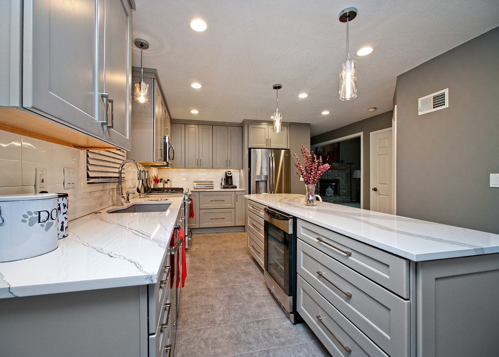 This is an example of a medium sized modern l-shaped kitchen/diner in Kansas City with a submerged sink, shaker cabinets, grey cabinets, white splashback, stainless steel appliances and an island.