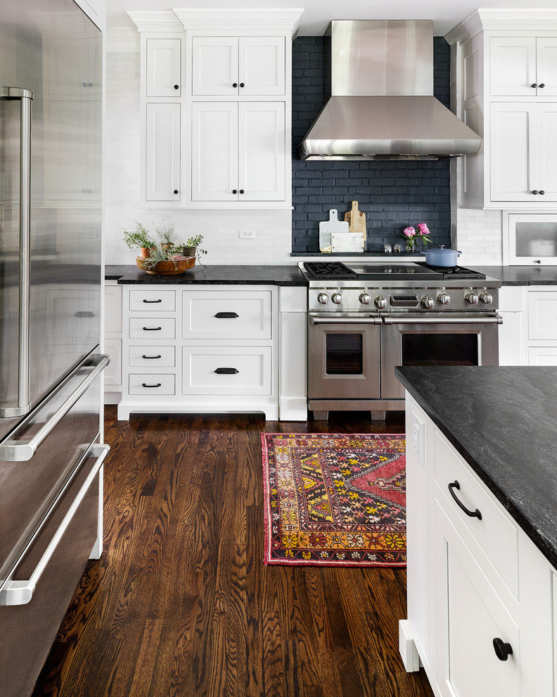 Design ideas for a large traditional kitchen/diner in Chicago with a belfast sink, beaded cabinets, white cabinets, granite worktops, white splashback, marble splashback, stainless steel appliances, dark hardwood flooring, multiple islands and brown floors.