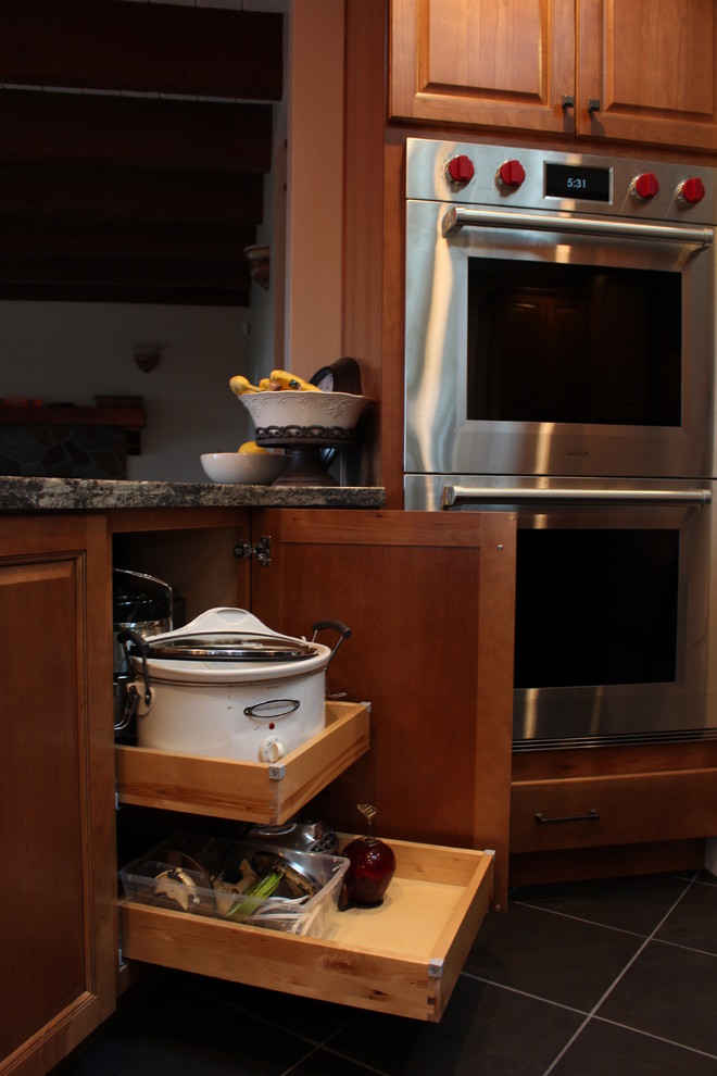 Exempel på ett stort klassiskt kök och matrum, med en undermonterad diskho, luckor med upphöjd panel, skåp i mellenmörkt trä, bänkskiva i kvarts, beige stänkskydd, stänkskydd i travertin, svarta vitvaror, skiffergolv, en köksö och grått golv