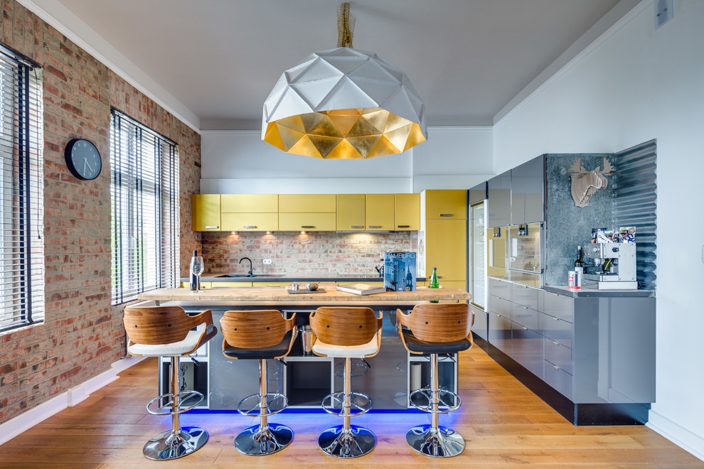 Expansive contemporary l-shaped enclosed kitchen in Hamburg with flat-panel cabinets, an island, a built-in sink, yellow cabinets, brown splashback, stone tiled splashback, integrated appliances and medium hardwood flooring.