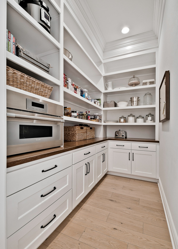 Exempel på ett stort amerikanskt vit vitt kök, med luckor med upphöjd panel, vita skåp, bänkskiva i kvartsit, vitt stänkskydd, rostfria vitvaror, ljust trägolv och en köksö