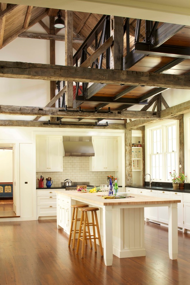 Foto på ett stort lantligt l-kök, med luckor med infälld panel, vita skåp, bänkskiva i täljsten, vitt stänkskydd, stänkskydd i tunnelbanekakel, rostfria vitvaror, mellanmörkt trägolv och en köksö
