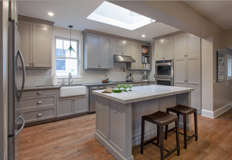 Inspiration for a large traditional grey and white u-shaped kitchen/diner in DC Metro with a belfast sink, shaker cabinets, grey cabinets, grey splashback, mosaic tiled splashback, stainless steel appliances, medium hardwood flooring, an island and brown floors.