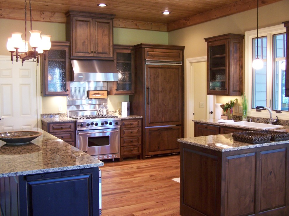 Cette image montre une cuisine ouverte craftsman en U et bois foncé avec un plan de travail en granite, un électroménager en acier inoxydable et un placard avec porte à panneau surélevé.
