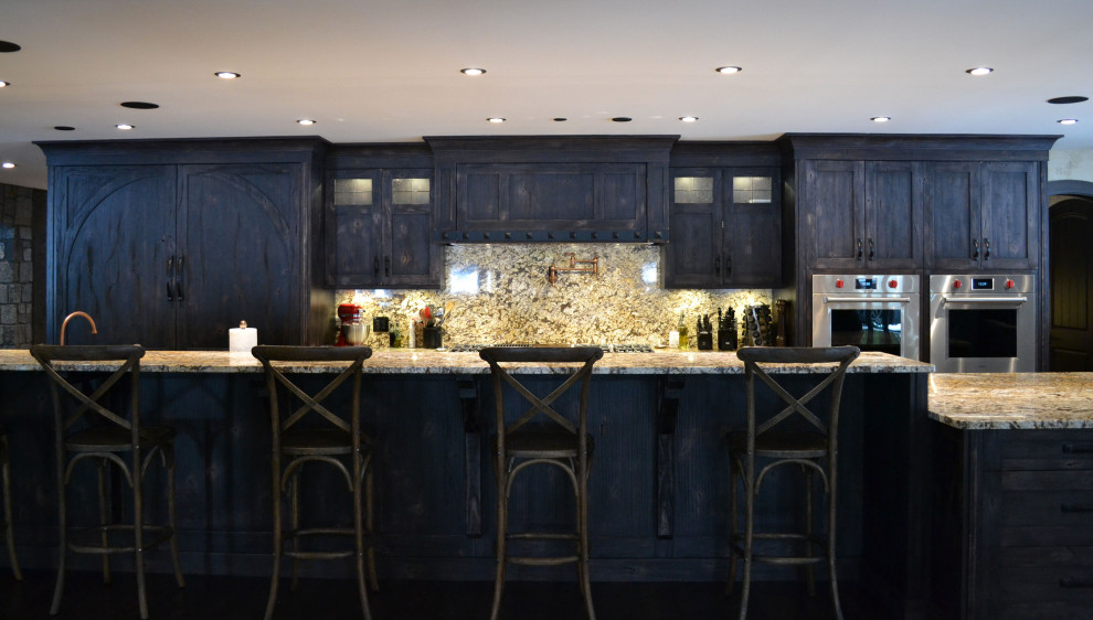 This is an example of a rustic open plan kitchen in Vancouver with flat-panel cabinets, distressed cabinets, granite worktops, granite splashback, stainless steel appliances and multiple islands.