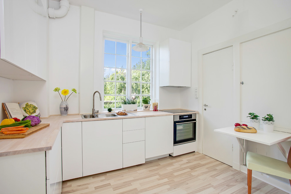 Exempel på ett litet skandinaviskt kök, med släta luckor, vita skåp, träbänkskiva, rostfria vitvaror, ljust trägolv och en dubbel diskho