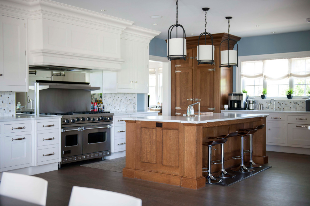 Inspiration for a large traditional l-shaped kitchen in New York with a belfast sink, shaker cabinets, white cabinets, grey splashback, porcelain splashback, stainless steel appliances, dark hardwood flooring, an island, brown floors and white worktops.