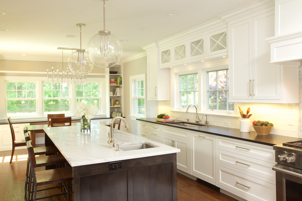 Inspiration for a large timeless u-shaped medium tone wood floor kitchen remodel in New York with an undermount sink, recessed-panel cabinets, white cabinets, quartz countertops, white backsplash, ceramic backsplash, paneled appliances and an island