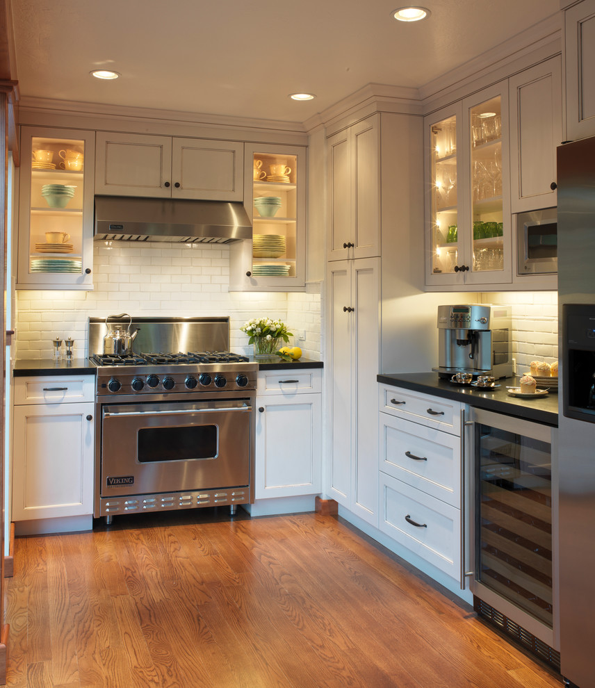 Inspiration for a timeless u-shaped enclosed kitchen remodel in San Francisco with subway tile backsplash, stainless steel appliances, glass-front cabinets, white cabinets and white backsplash