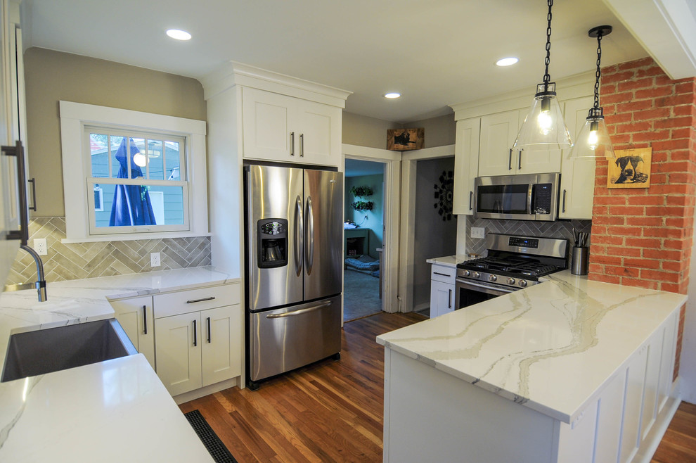 Mid-sized trendy l-shaped light wood floor eat-in kitchen photo in Denver with a farmhouse sink, shaker cabinets, white cabinets, quartzite countertops, gray backsplash, porcelain backsplash, stainless steel appliances, a peninsula and white countertops