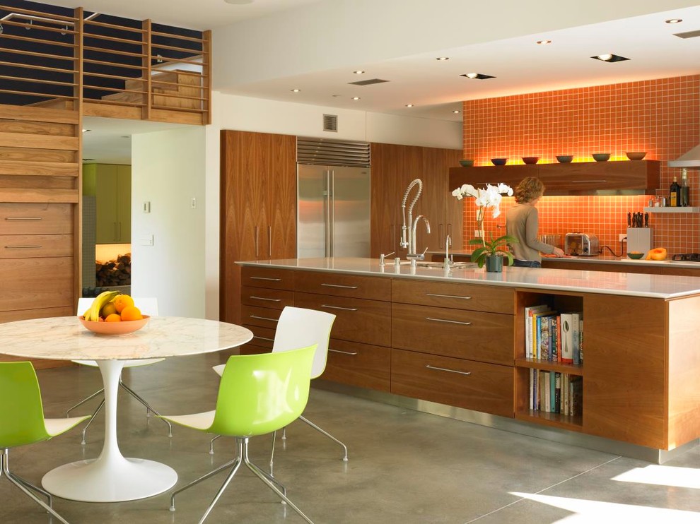 Идея дизайна: кухня в стиле ретро с обеденным столом, врезной мойкой, плоскими фасадами, фасадами цвета дерева среднего тона, оранжевым фартуком, техникой из нержавеющей стали, бетонным полом и островом