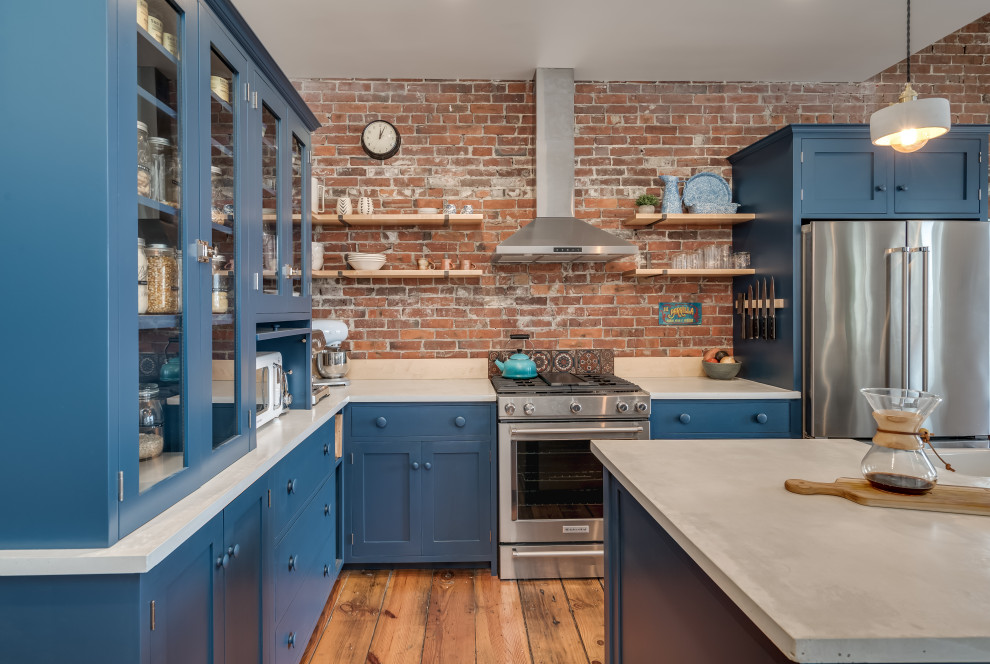 На фото: угловая кухня в стиле неоклассика (современная классика) с синими фасадами, фартуком из кирпича, техникой из нержавеющей стали, паркетным полом среднего тона, островом и фасадами в стиле шейкер