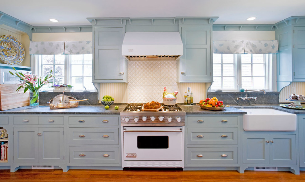 Inspiration for a small coastal galley medium tone wood floor enclosed kitchen remodel in Other with a farmhouse sink, flat-panel cabinets, blue cabinets, soapstone countertops, white backsplash, mosaic tile backsplash and stainless steel appliances