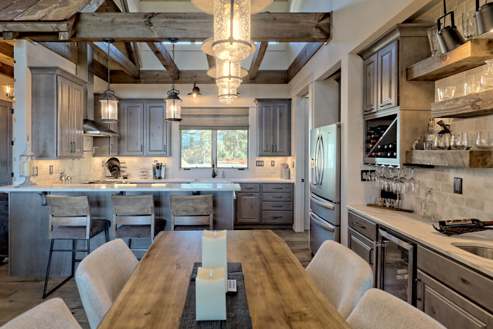 This is an example of a small rural u-shaped open plan kitchen in Atlanta with a belfast sink, raised-panel cabinets, light wood cabinets, engineered stone countertops, white splashback, travertine splashback, stainless steel appliances, a breakfast bar, brown floors and white worktops.
