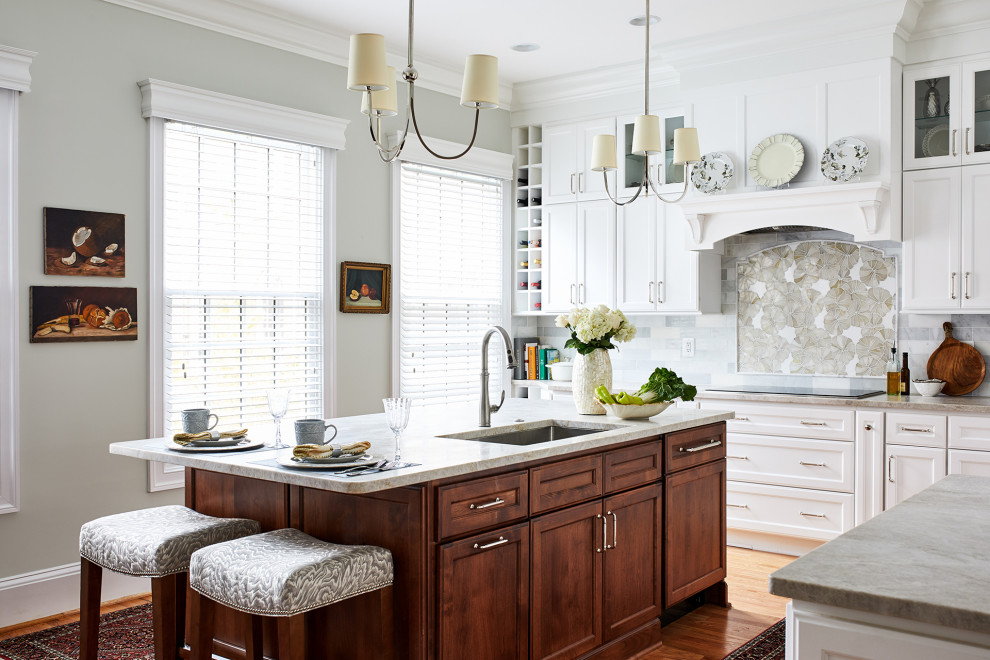 Inredning av ett klassiskt avskilt, stort vit vitt l-kök, med en undermonterad diskho, luckor med infälld panel, vita skåp, grått stänkskydd, en köksö och beiget golv