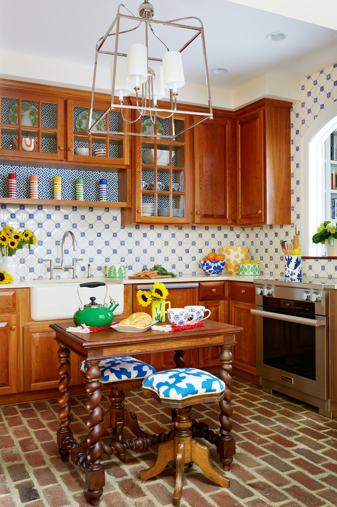 Design ideas for a rural u-shaped enclosed kitchen in DC Metro with a belfast sink, medium wood cabinets, blue splashback, ceramic splashback, stainless steel appliances, brick flooring, an island, raised-panel cabinets and brown floors.