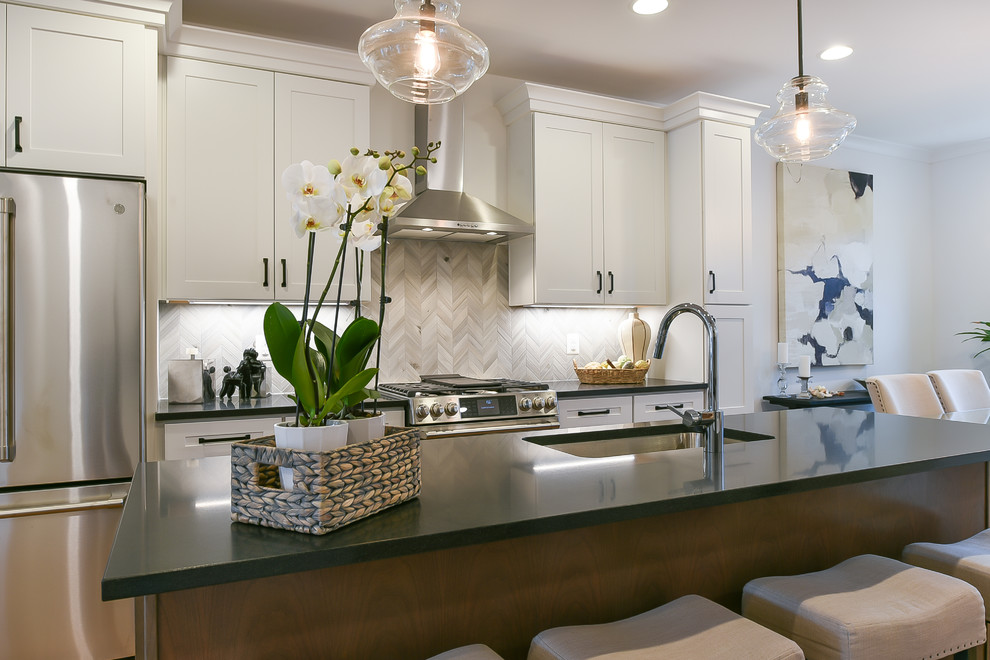 Example of an urban medium tone wood floor kitchen design in DC Metro with an undermount sink, recessed-panel cabinets, white cabinets, granite countertops, gray backsplash, mosaic tile backsplash, stainless steel appliances, an island and black countertops