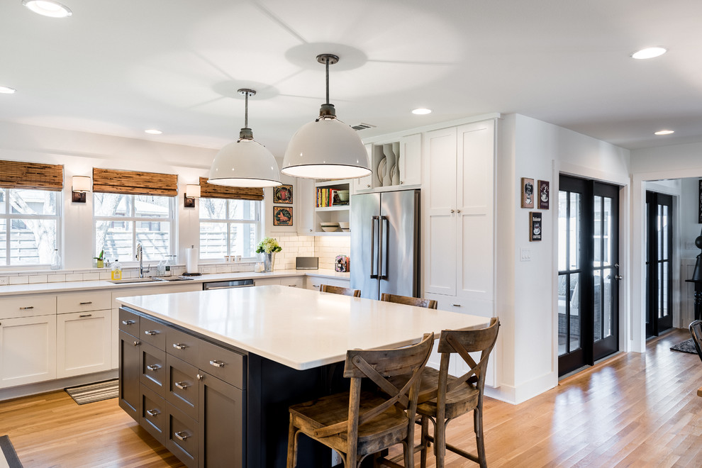 Large traditional u-shaped kitchen/diner in Austin with a double-bowl sink, recessed-panel cabinets, white cabinets, engineered stone countertops, white splashback, metro tiled splashback, stainless steel appliances, medium hardwood flooring and an island.