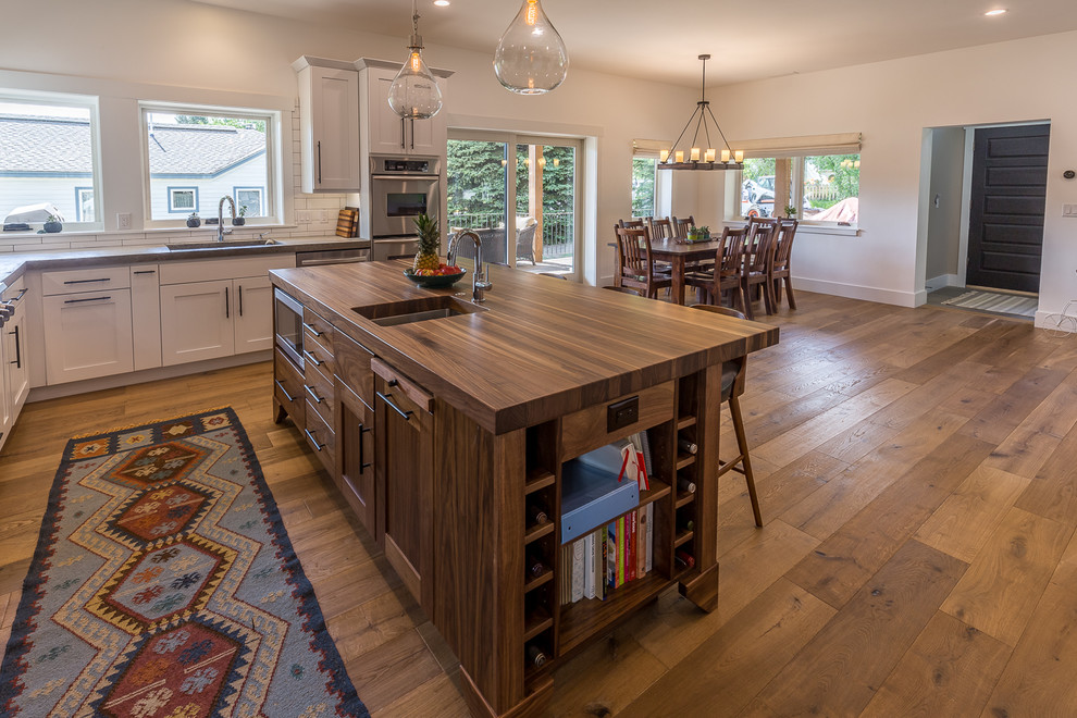 Country l-shaped medium tone wood floor open concept kitchen photo in Denver with a single-bowl sink, white cabinets, concrete countertops, white backsplash, subway tile backsplash, stainless steel appliances and an island