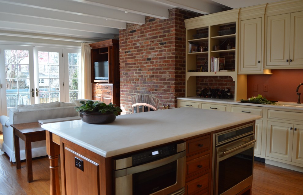 Inredning av ett klassiskt mellanstort kök, med luckor med profilerade fronter, beige skåp, marmorbänkskiva, rostfria vitvaror, mellanmörkt trägolv, en köksö, en undermonterad diskho och orange stänkskydd
