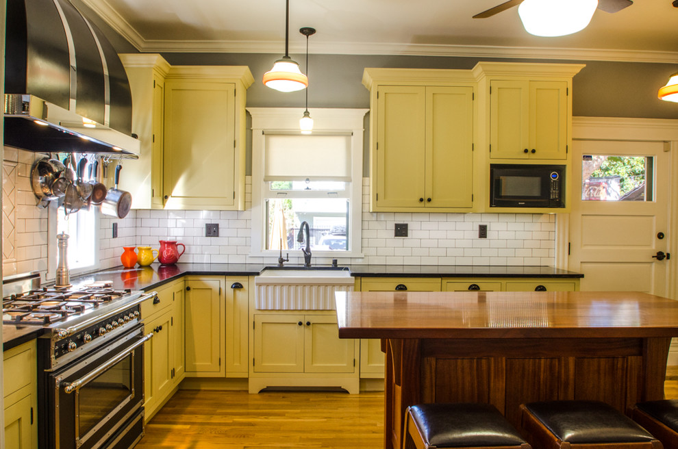 Mittelgroße Landhausstil Wohnküche in U-Form mit Landhausspüle, Schrankfronten im Shaker-Stil, gelben Schränken, Granit-Arbeitsplatte, Küchenrückwand in Weiß, Rückwand aus Porzellanfliesen, braunem Holzboden und Kücheninsel in Orange County