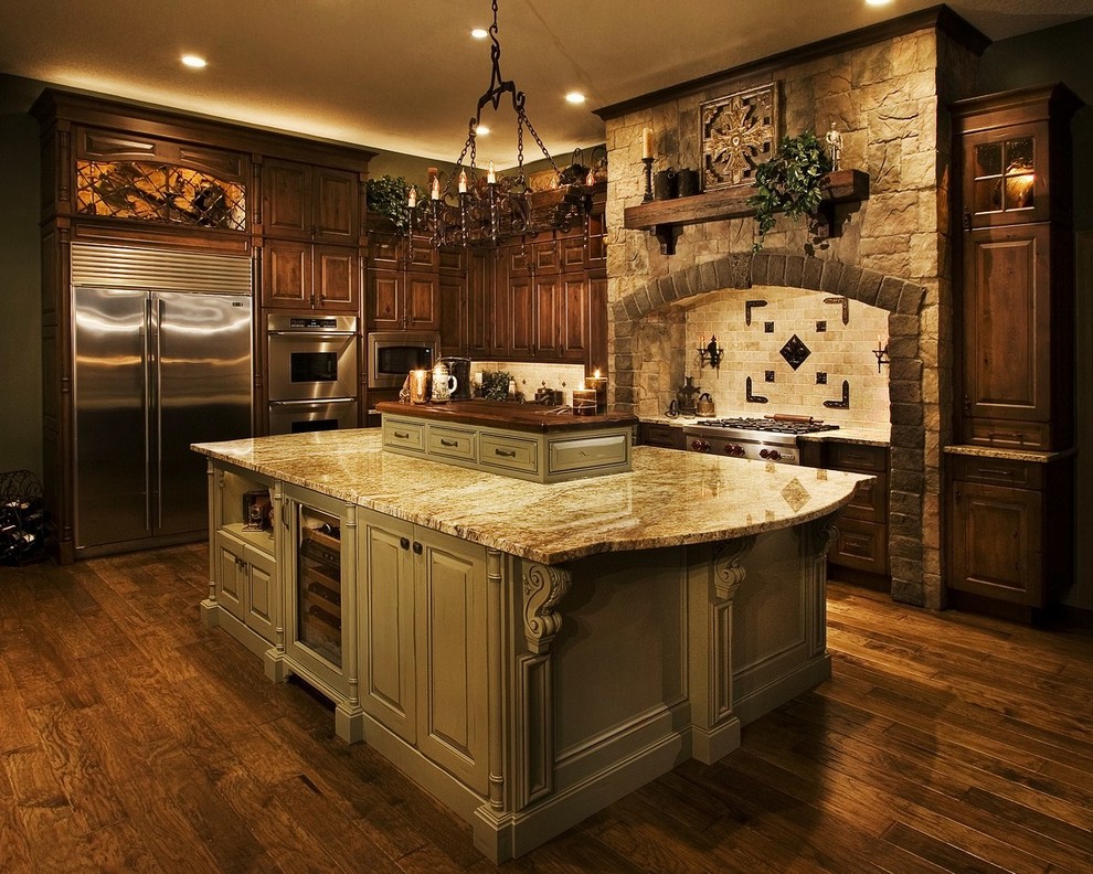 Inredning av ett klassiskt stort kök, med en rustik diskho, luckor med upphöjd panel, gröna skåp, granitbänkskiva, beige stänkskydd, stänkskydd i stenkakel, rostfria vitvaror, mörkt trägolv, en köksö och brunt golv