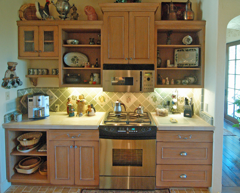 Medelhavsstil inredning av ett stort kök, med en nedsänkt diskho, luckor med profilerade fronter, skåp i mellenmörkt trä, kaklad bänkskiva, grönt stänkskydd, stänkskydd i keramik, rostfria vitvaror, tegelgolv och en köksö