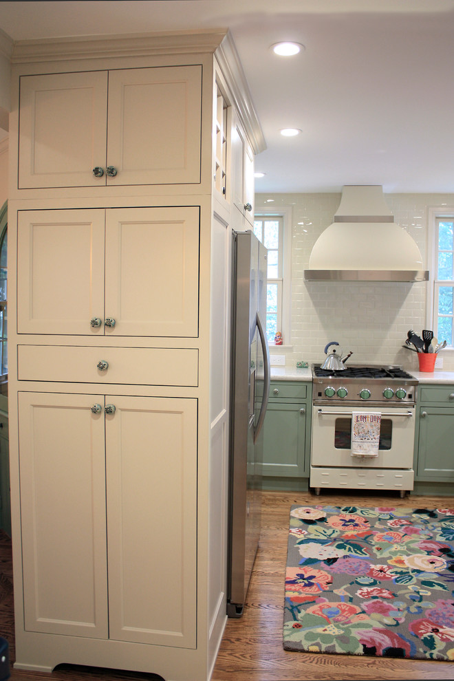 Example of a small eclectic u-shaped light wood floor enclosed kitchen design in San Francisco with a farmhouse sink, shaker cabinets, green cabinets, quartz countertops, white backsplash, ceramic backsplash and white appliances