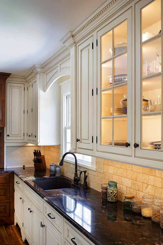 Klassisk inredning av ett stort kök, med mellanmörkt trägolv, en undermonterad diskho, luckor med profilerade fronter, vita skåp, granitbänkskiva, beige stänkskydd, stänkskydd i stenkakel, rostfria vitvaror och en köksö