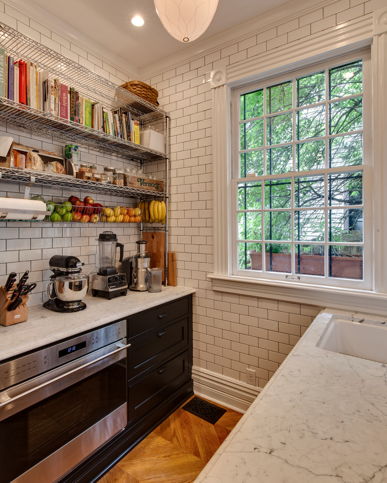 На фото: параллельная, отдельная кухня в стиле неоклассика (современная классика) с черными фасадами, белым фартуком и фартуком из плитки кабанчик с