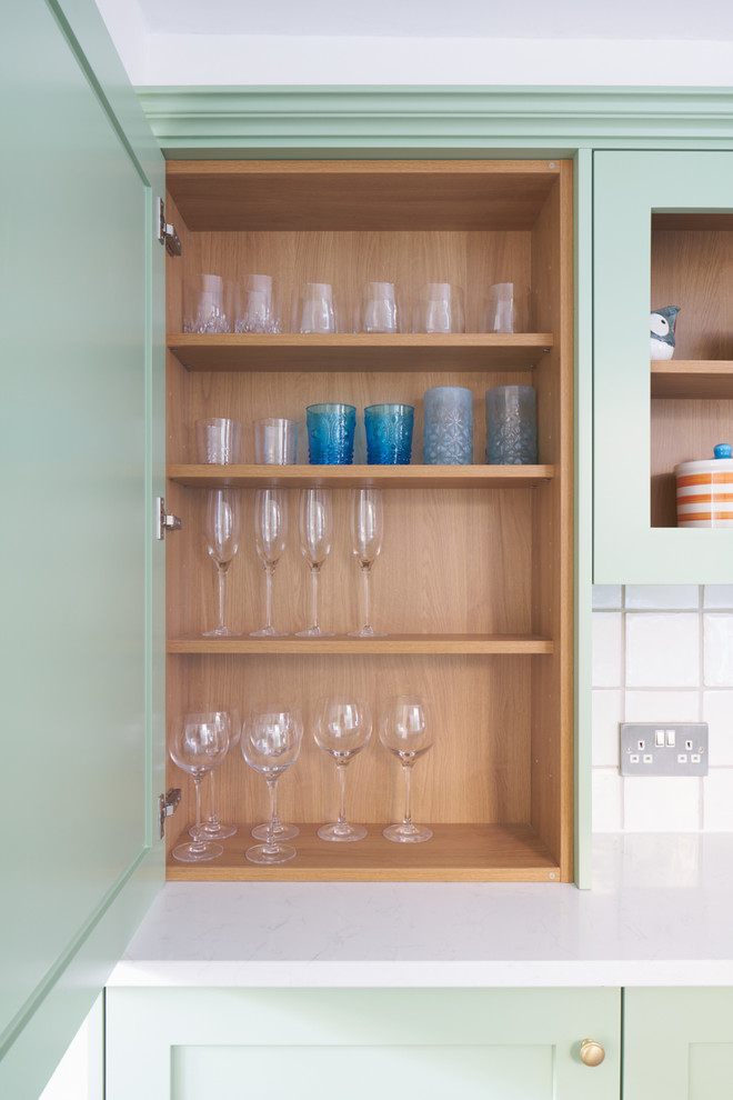 Photo of a small contemporary galley kitchen in London with a belfast sink, shaker cabinets, green cabinets, quartz worktops, white splashback, ceramic splashback, integrated appliances and terracotta flooring.
