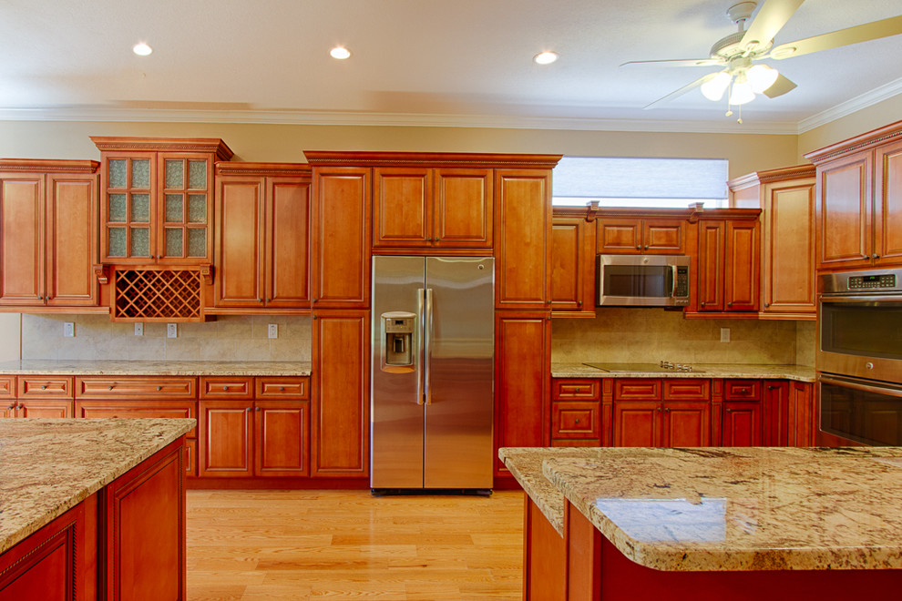 Eat-in kitchen - large traditional galley medium tone wood floor eat-in kitchen idea in Tampa with an undermount sink, beaded inset cabinets, medium tone wood cabinets, granite countertops, beige backsplash, ceramic backsplash, stainless steel appliances and an island