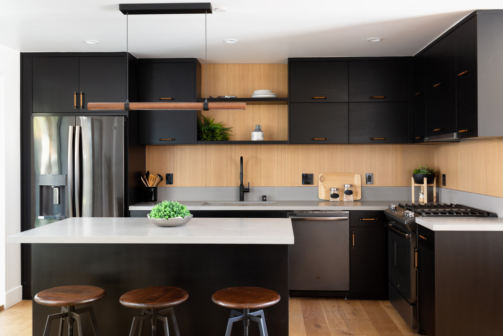 Moderne Küche in L-Form mit Unterbauwaschbecken, Kassettenfronten, schwarzen Schränken, Küchengeräten aus Edelstahl, braunem Holzboden, braunem Boden und grauer Arbeitsplatte in Los Angeles