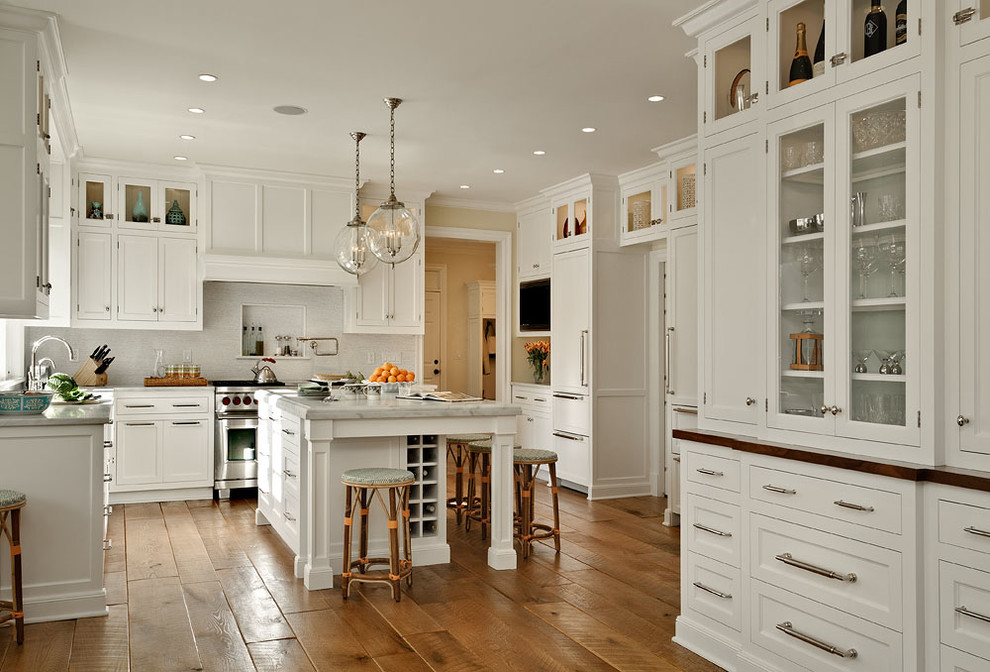 Klassische Küche in U-Form mit Landhausspüle, Schrankfronten im Shaker-Stil, weißen Schränken, Küchenrückwand in Weiß, Küchengeräten aus Edelstahl, braunem Holzboden und Kücheninsel in New York
