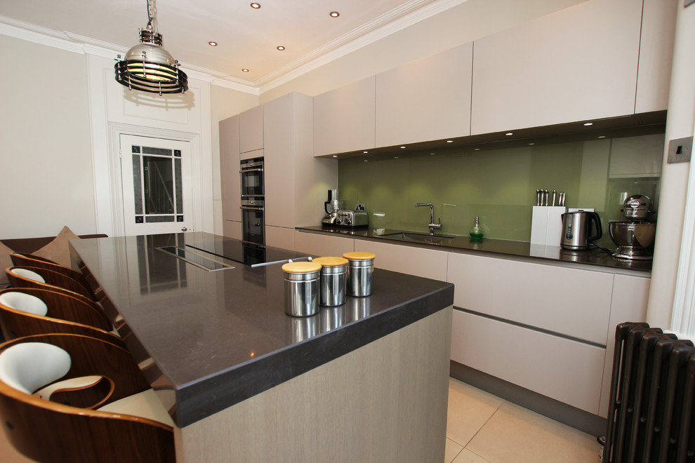 Photo of a contemporary kitchen in London with grey cabinets, green splashback, glass sheet splashback and an island.