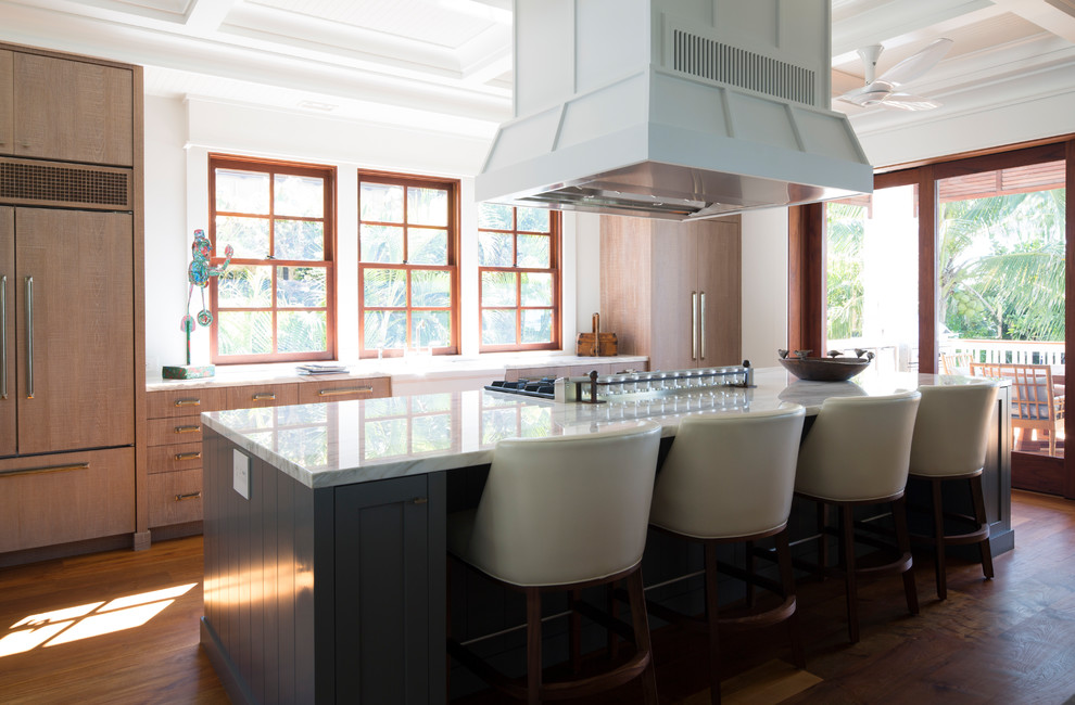 Photo of a world-inspired kitchen in Hawaii with a belfast sink, flat-panel cabinets, marble worktops, integrated appliances, an island, brown floors, white worktops, medium hardwood flooring and medium wood cabinets.