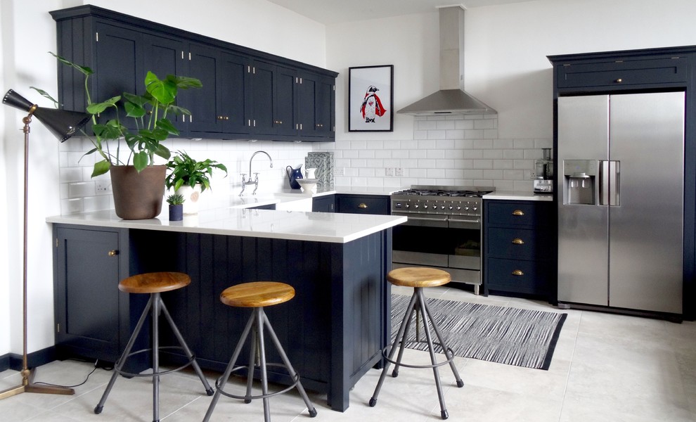 Inspiration for a medium sized contemporary u-shaped open plan kitchen in London with a belfast sink, shaker cabinets, blue cabinets, composite countertops, white splashback, ceramic splashback, stainless steel appliances, ceramic flooring, a breakfast bar, grey floors and white worktops.