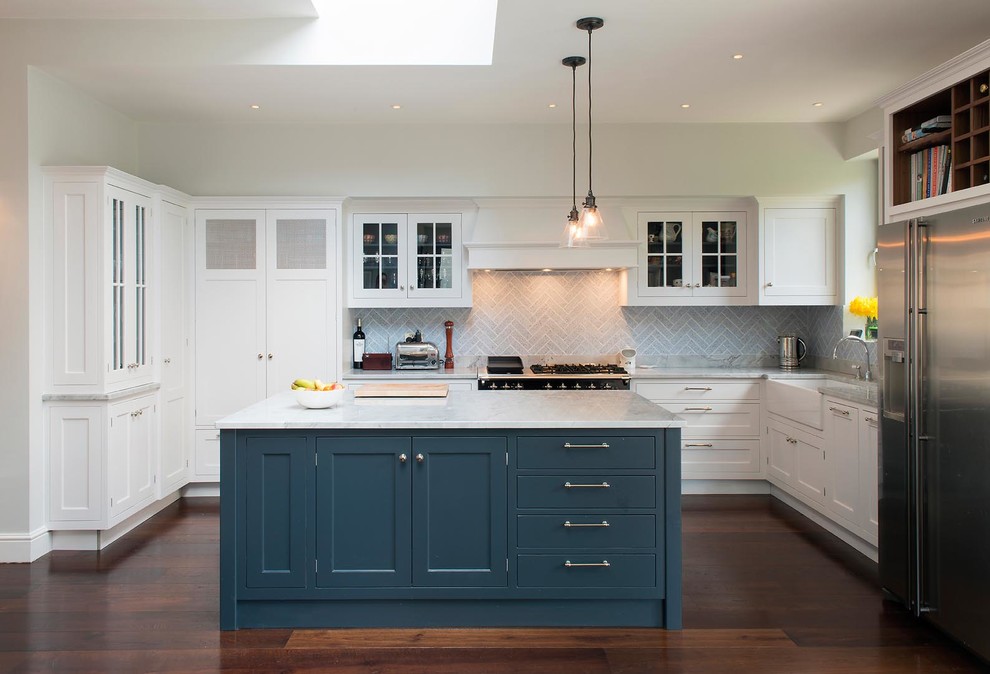 Inspiration for a transitional u-shaped dark wood floor kitchen remodel in London with a farmhouse sink, shaker cabinets, white cabinets, gray backsplash, stainless steel appliances and an island