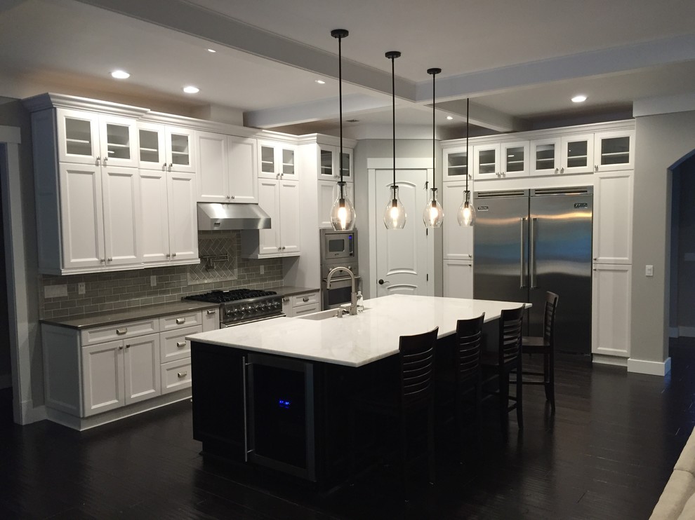 Example of a large trendy l-shaped dark wood floor and black floor open concept kitchen design in Seattle with white cabinets, quartzite countertops, gray backsplash, an island, a farmhouse sink, recessed-panel cabinets, subway tile backsplash and stainless steel appliances