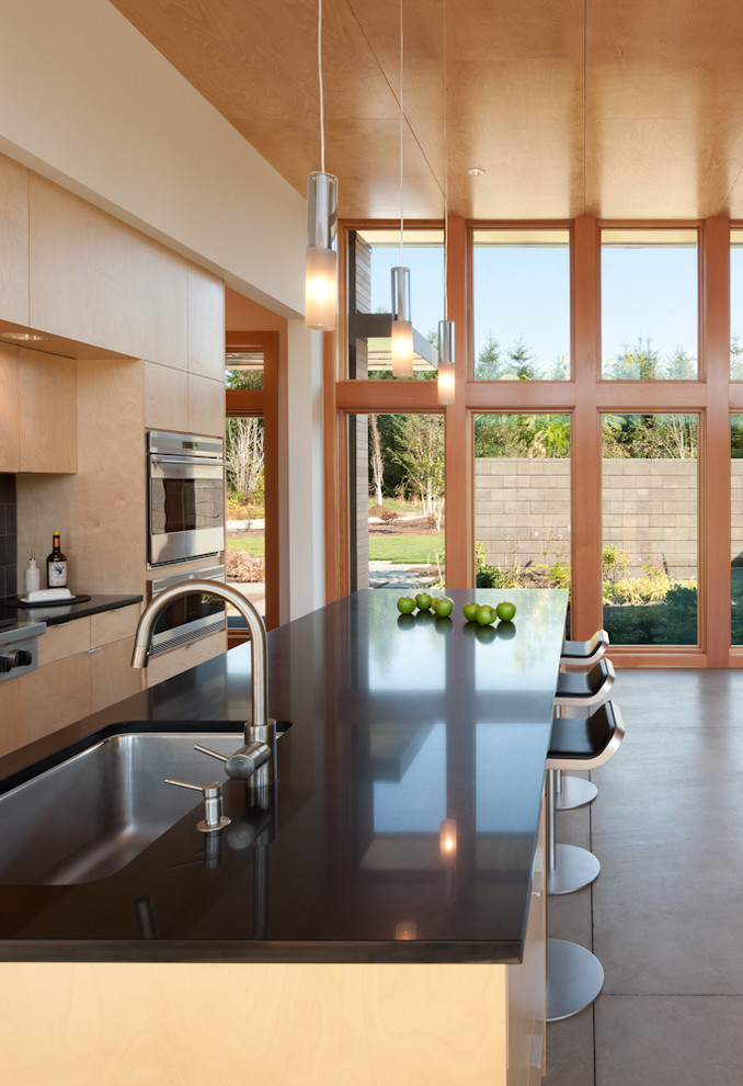 Diseño de cocina moderna con fregadero bajoencimera, armarios con paneles lisos, puertas de armario de madera clara y electrodomésticos de acero inoxidable