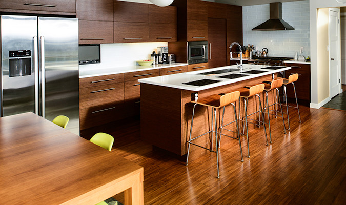 This is an example of a medium sized retro l-shaped open plan kitchen in Seattle with a submerged sink, flat-panel cabinets, medium wood cabinets, engineered stone countertops, white splashback, glass tiled splashback, stainless steel appliances, medium hardwood flooring, an island and brown floors.