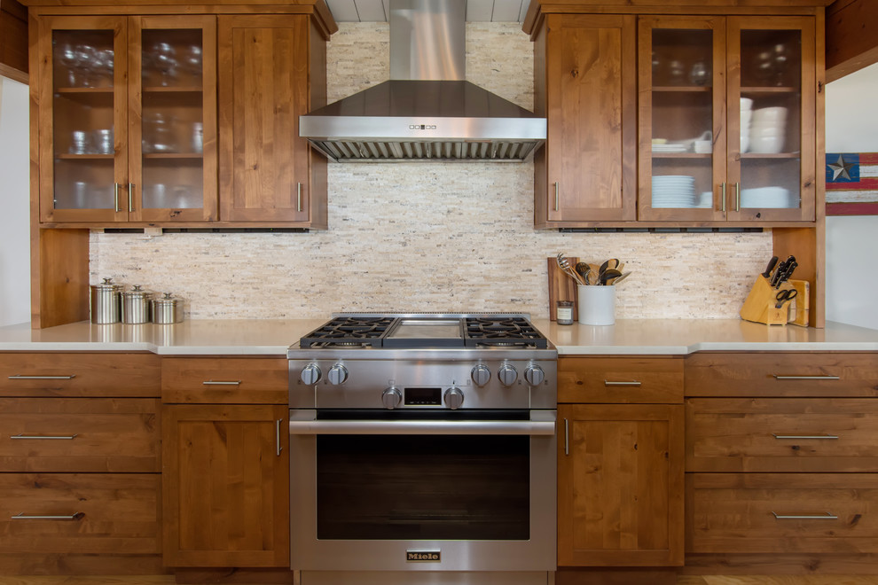 This is an example of a large classic galley kitchen/diner in Seattle with a single-bowl sink, shaker cabinets, medium wood cabinets, engineered stone countertops, beige splashback, stone tiled splashback, stainless steel appliances, medium hardwood flooring, an island and brown floors.