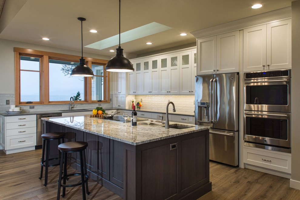 Kitchen - large transitional medium tone wood floor kitchen idea in Seattle with an undermount sink, shaker cabinets, white cabinets, granite countertops, white backsplash, subway tile backsplash, stainless steel appliances and an island