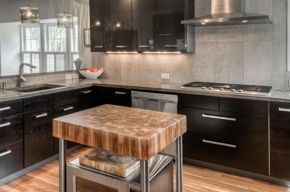 Example of a mid-sized trendy u-shaped light wood floor and beige floor eat-in kitchen design in Omaha with a single-bowl sink, flat-panel cabinets, black cabinets, concrete countertops, gray backsplash, porcelain backsplash, stainless steel appliances and an island