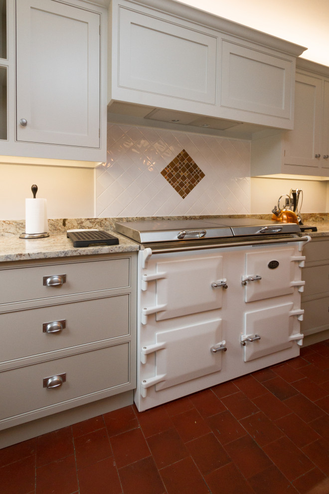 グロスタシャーにある広いトラディショナルスタイルのおしゃれなキッチン (ダブルシンク、シェーカースタイル扉のキャビネット、グレーのキャビネット、御影石カウンター、白いキッチンパネル、セラミックタイルのキッチンパネル、シルバーの調理設備、テラコッタタイルの床、赤い床、緑のキッチンカウンター) の写真