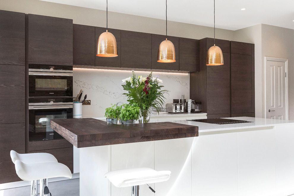 Moderne Küche mit flächenbündigen Schrankfronten, dunklen Holzschränken, Küchenrückwand in Weiß, schwarzen Elektrogeräten und Kücheninsel in London