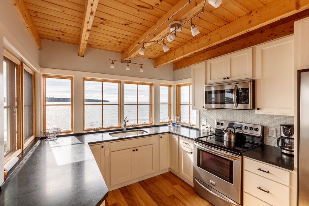 Inspiration for a small coastal u-shaped medium tone wood floor enclosed kitchen remodel in Portland Maine with an undermount sink, shaker cabinets, white cabinets, glass countertops, white backsplash, matchstick tile backsplash, stainless steel appliances and no island