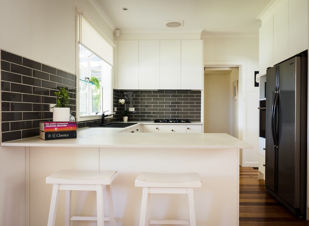 Bild på ett litet funkis vit vitt kök, med en dubbel diskho, bänkskiva i kvarts, grått stänkskydd, stänkskydd i keramik, släta luckor, rostfria vitvaror, mörkt trägolv och brunt golv