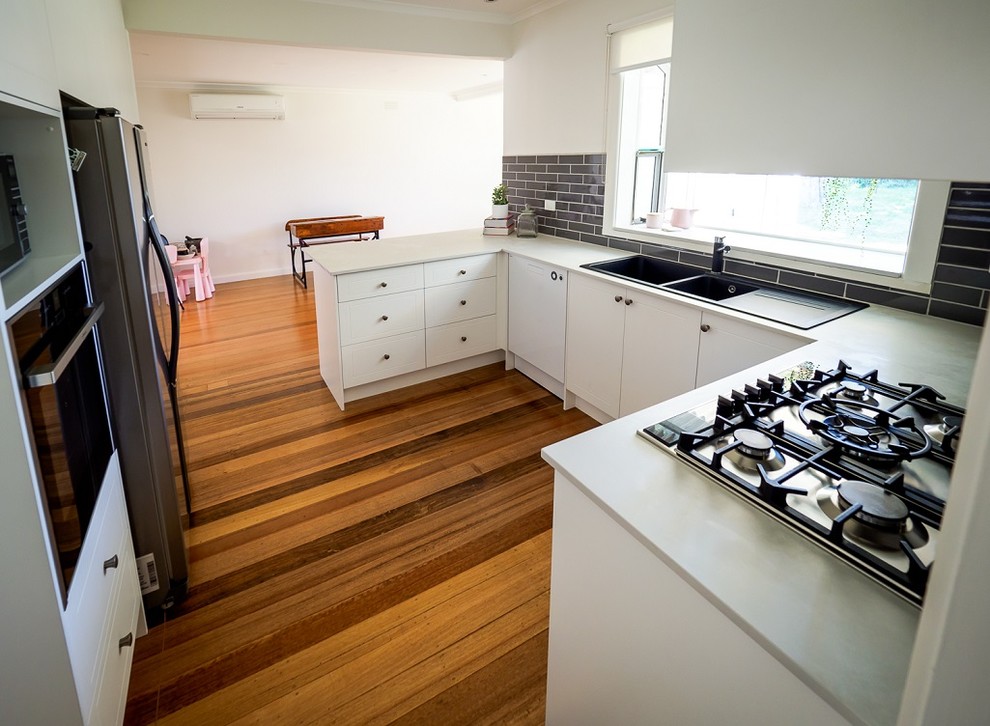 This is an example of a small contemporary u-shaped kitchen/diner in Melbourne with a double-bowl sink, engineered stone countertops, grey splashback, ceramic splashback, flat-panel cabinets, stainless steel appliances, dark hardwood flooring, no island, brown floors and white worktops.